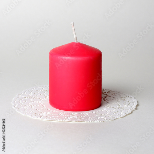 Single thick pink aromatic candle on white openwork paper napkin on gray background side closeup view 