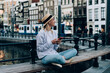 © BullRun - Smiling woman using smartphone sitting on bench near channel