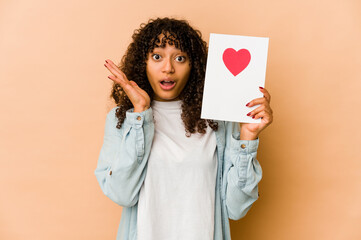 Wall Mural - Young african american afro woman holding a valentines day card surprised and shocked.