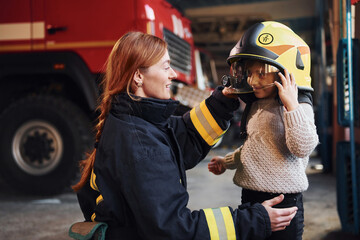 Happy little girl is with female firefighter in protective uniform