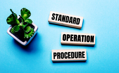 STANDARD OPERATION PROCEDURE is written on wooden blocks on a light blue background near a flower in a pot