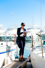 Female yachting dealer in marine blue suit holding notepad, standing outside a luxury sailboat, Heraklion, Crete, Greece