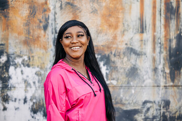 Beautiful African American teenage girl with long hair and a pink magenta jacket standing  outside in an urban city setting looking off to the side