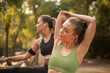 © LOUIS CHRISTIAN/Westend61 - Young sportswoman stretching while exercising with friend in background outdoors