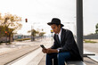 © VITTA GALLERY/Westend61 - Young man in hat using smart phone at bus stop on sunny day