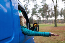Mid Adult Woman Leaning Hand Out Of Window From Camper Van On Rainy Day