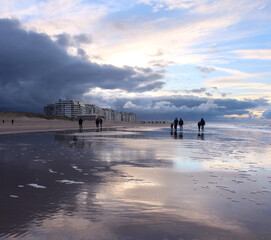 Silhouetted people walking on the sandy beach during a winters sunset at Wenduine, West Flanders, Belgium