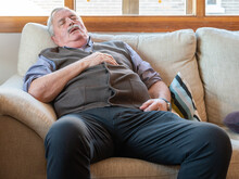 Tired Elderly Male Fall Asleep On A Comfortable Couch In The Living Room