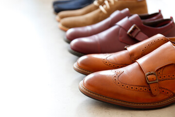 Poster - Bunch of different style men's shoes in a row isolated on white background. Close up shot chukka boots, single and double monk strap oxfords, brown and burgundy shoes. Top view, copy space, flat lay.