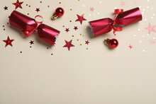Open Red Christmas Cracker And Decorations With Shiny Confetti On Beige Background, Flat Lay. Space For Text