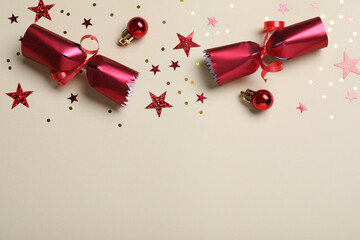 Wall Mural - Open red Christmas cracker and decorations with shiny confetti on beige background, flat lay. Space for text