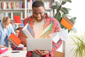 Wall Mural - African-American student with laptop reading book online in library