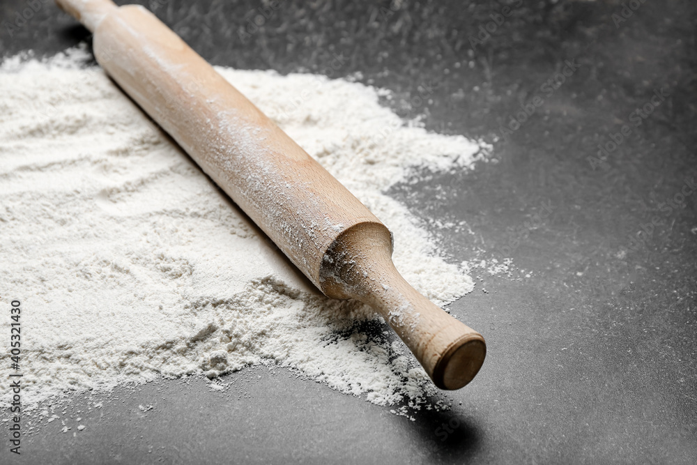Wooden rolling pin and flour on dark background