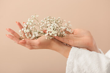 Hands of young woman in bathrobe and with beautiful flowers on color background