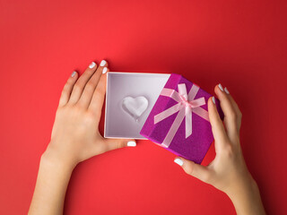 The girl's hands open a gift box with a glass heart inside.