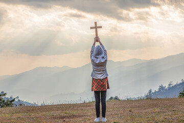 Child praying to the GOD while holding a crucifix  of Jesus Christ at sunlight background.Easter Sunday concept: