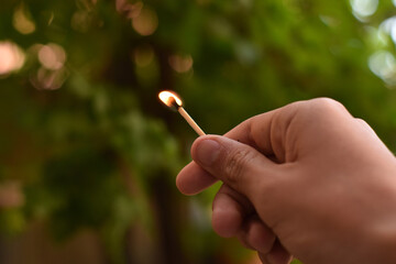 Poster - Closeup shot of a hand holding burning matchstick with smoke against a green bokeh background