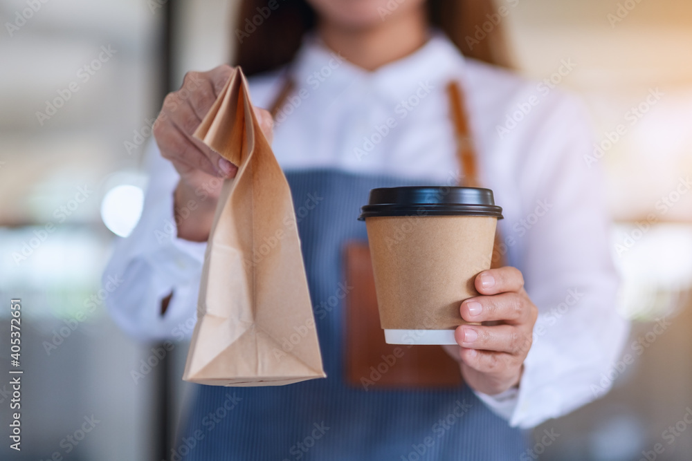 A waitress holding and serving paper cup of coffee and takeaway food in paper bag to customer in a shop - obrazy, fototapety, plakaty 
