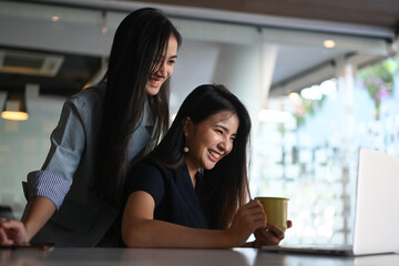 Two happy young woman working together on new project and using laptop computer at co working area.