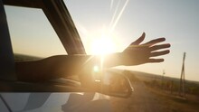 free girl hand out of the window rides a car wind in the face. concept car travel on the road. girl stretches her hand out of the car window sun glare sunset movement. driver hand out of the window