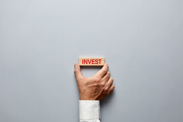 Wall Mural - Businessman hand holding a wooden block with the word invest on it. Decision of financial investment in business
