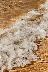 Wall Mural - Vertical shot of foam waves hitting a sandy seashore
