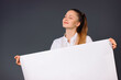 © Viorel - A satisfied young business woman holds a blank white banner in her hands for your advertisement. Grey background.
