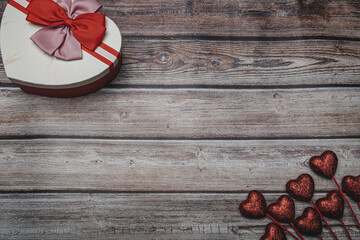 Poster - Heart-shaped gift box with bow ties and glitter hearts on stick on wooden table with copy space