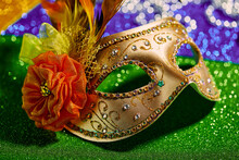 Festive, Colorful Mardi Gras Or Carnivale Mask And Beads On Golden, Green And Purple Background, Close Up. Venetian Masks. Party Invitation, Greeting Card, Venetian Carnivale Celebration Concept.
