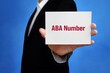 ABA Number. Lawyer (man) holding a card in his hand. Text on the sign presents term. Blue background.