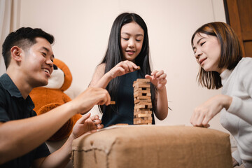 Asian mother, father, and pretty daughter playing wooden block tower together in playtime in living room. Happy and fun family educational at home concept.