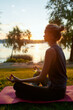 © Svitlana - Side view of a young woman wearing sport clothes doing yoga in nature, sitting in lotus pose and meditating
