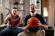© JustLife - Two young friends enjoying at home. Men drinking beer and watching sports game on tv..