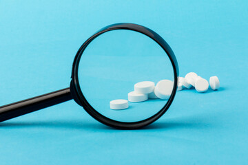 Wall Mural - Concept - pharmaceutical testing, testing of medicines, magnifying glass, tablets on a blue background. Doping control.