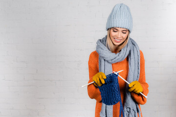 Canvas Print - Young positive woman in warm gloves an sweater knitting with wool thread on white background