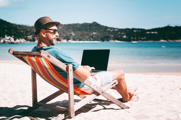 Wall Mural - attractive young man with laptop working on the beach. freedom, remote work, freelancer, technology,