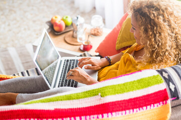 Wall Mural - Adult young woman at home use laptop computer lay down on the sofa - image of people and home work job technology with internet connection - happy free people in alternative office smart working