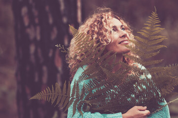 Wall Mural - Portrait of happy cheerful woman holding big leaf in the forest with trees in background - concept of nature protection and save planet earth from deforestation - nature outdoor respect