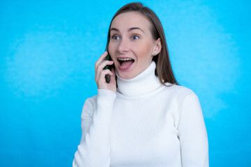 Happy woman talking by smartphone and looking away over blue background