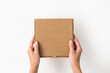 © Iryna_B - female hands holding a small cardboard box on a white background. packaging and delivery concept, top view