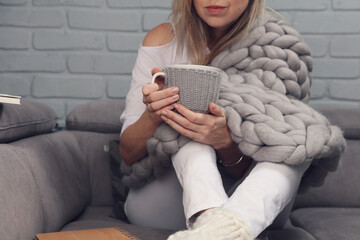 Cozy Woman covered with warm soft merino wool blanket drinking coffee at home. Comfort lifestyle.