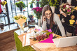 © Dragana Gordic - Smiling Woman Florist Small Business Flower Shop Owner. She is using her telephone and laptop to take orders for her store. Female gardener noting client order during mobile phone conversation