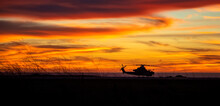 Silhouette Of An Attack Helicopter At Against A Dramatic Cloudy Sky At Sunset Or Sunrise