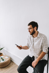 Wall Mural - Portrait of young cheerful caucasian man in glasses and earphones using mobile phone.