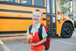 © anoushkatoronto - Happy laughing smiling Caucasian boy student by yellow bus on first September day. Hard of hearing child kid eating apple fruit at school yard outdoors. Education and back to school in Autumn Fall.