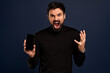 You will have problems man. Portrait of angry confused aggressive in bad mood guy shouting threatening at the camera, holding his smartphone, isolated on Pacific Blue background