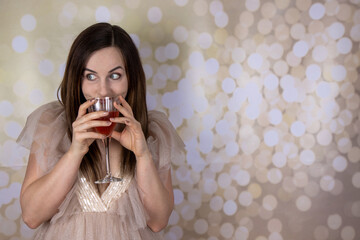 A fairy tail concept of an attractive woman in a glittery retro style party Christmas or wedding dress looking shocked and holding a glass of rose wine on a gold background