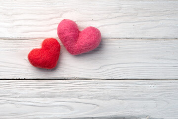 Two woolen handmade hearts on the white textured wooden boards