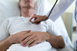 © My Ocean studio - Young modern confident woman doctor in a white coat with a stethoscope is examining the patient's feelings while he is lying on the bed in the hospital ward.