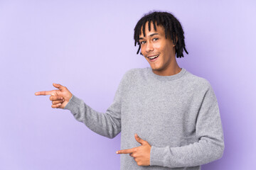 Wall Mural - Young african american man isolated on purple background surprised and pointing side